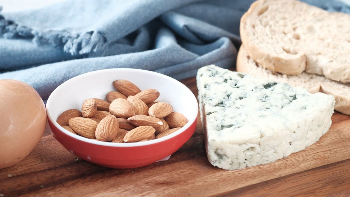 a bowl of almonds, bread, and an egg on a cutting board